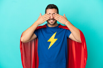 Super Hero caucasian man isolated on blue background covering eyes by hands