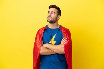 Young handsome caucasian man isolated on yellow background in superhero costume with arms crossed © luismolinero
