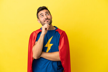 Young handsome caucasian man isolated on yellow background in superhero costume and thinking © luismolinero