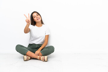 Teenager girl sitting on the floor smiling and showing victory sign