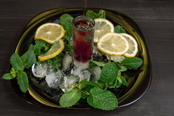 Cherry liqueur with mint and lemon on a black plate with ice