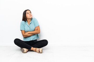 Teenager girl sitting on the floor making doubts gesture while lifting the shoulders