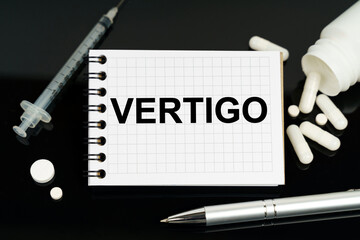 On the black surface are pills, a syringe and a notebook with the inscription - vertigo