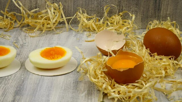 Chicken eggs, white and brown, raw and boiled, whole and cut in two, in eggshell and peeled, lie on a wooden table.