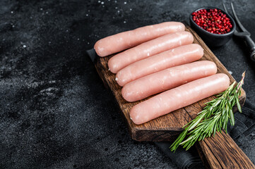 Fresh Raw chicken and turkey meat sausages on a wooden board with rosemary. Black background. Top...