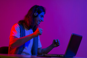 Funny guy gamer playing on a laptop. A young man with headphones is using a computer, playing...
