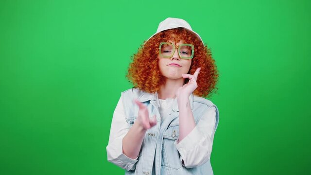 Cute positive redhead curly lady wearing eyeglasses and panama hat dancing, moving backward and gesturing gotcha