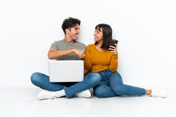 Young couple with a laptop and mobile sitting on the floor handshaking after good deal