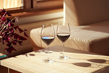 Two glasses of red wine on a table indoors in sunlight from the window