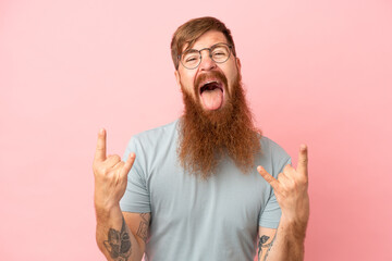 Young reddish caucasian man isolated on pink background making horn gesture