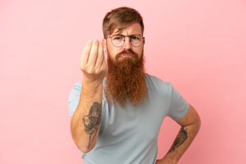 Young reddish caucasian man isolated on pink background making Italian gesture