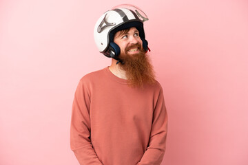Young reddish caucasian man with a motorcycle helmet isolated on pink background thinking an idea while looking up