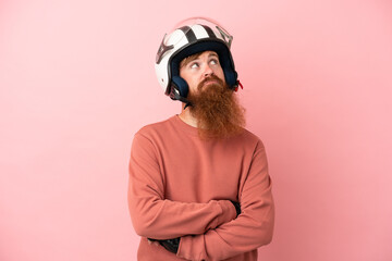 Young reddish caucasian man with a motorcycle helmet isolated on pink background and looking up