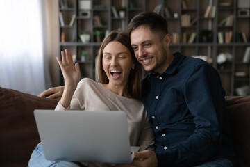 Happy young family couple waving hands, starting video call meeting with friends or family, using computer software application. cheerful millennial bloggers streaming stories for social networks.