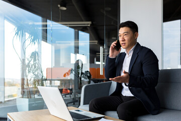 Thinking asian businessman businessman, talking on the phone working in a modern office, listening...