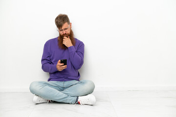 Young caucasian reddish man sitting on the floor isolated on white background thinking and sending a message