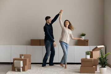 Happy sincere young family couple dancing to music in living room between carton parcels. Joyful...