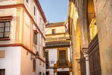 Facades of houses with tiled roofs and an ancient building with arches in the Old Town of Cordoba, Andalusia, Spain.