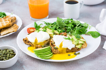 Healthy breakfast. Toast with poached eggs, slices of avocado, leaves and cherry tomatoes on a plate and juice and coffee on a served table. Flexetarian diet