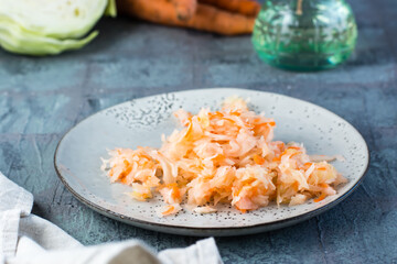 Fresh sauerkraut with carrots on a plate and vegetables on the table. Fermentation and a vegetarian diet