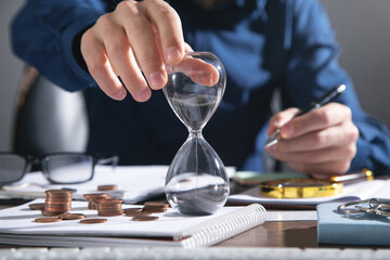 Fototapeta na wymiar Businessman holding hourglass. Coins and business objects on the desk
