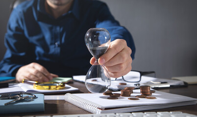 Businessman holding hourglass. Coins and business objects on the desk