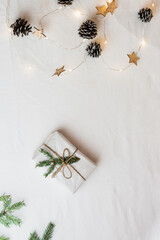 Minimalistic eco christmas. Gift wrapped in craft paper decorated with fir branches and a garland on a white cloth. Top and vertical view