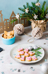 Freshly baked Christmas cookies with pink icing on a plate on a decorated table. Festive treat. Vertical view.