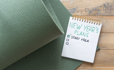 Notepad on the wooden background with the inscription - New year's plan - start yoga.