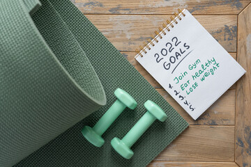 Notepad on the wooden background with the goals for 2022 - join gym, eat healthy, loose weight.