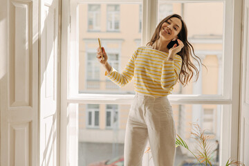 Beautiful european young woman is listening to pleasant voice message through headphones on phone....