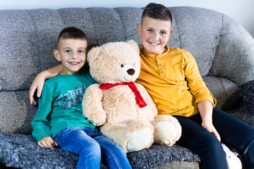 Cute, little boys sitting on the sofa with teddy bear having fun. Brothers love