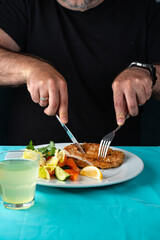 male hand eating from big dish German schnitzel with salad
