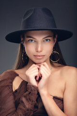 Fashionable studio portrait of a beautiful young girl in black hat on a grey background.