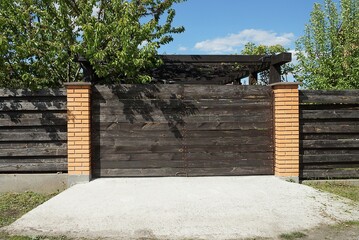 one closed brown private gate and part of the fence from wooden boards and bricks on the street