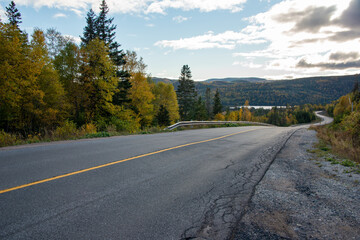 A long two lane paved road with a slight s curve and yellow line. The highway has tall orange,...
