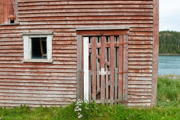 The corner of a two story vintage wooden barn with a single glass pane window and a wood door....