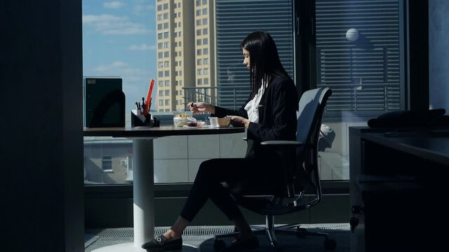 Business woman eats at the workplace, in a modern beautiful office near the panoramic window and flirts with the workers, builders in the window