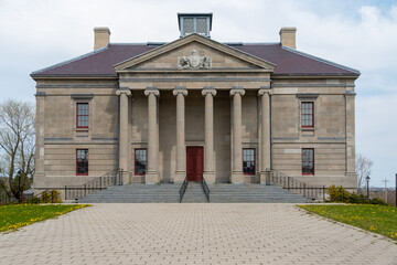 Obraz premium A wide brick entrance to a large courthouse, justice, or government style building. There's a tall red door, grey marble steps, black handrails, tall windows, round pillars, and a beige exterior wall.