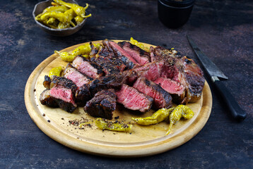 Traditional barbecue dry aged wagyu porterhouse beef steak bistecca alla Fiorentina sliced and served with pepperoni as close-up on a rustic wooden board