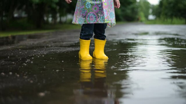 Children's yellow rubber boots stomp on a puddle on a rainy day. A child playing in the rain outside