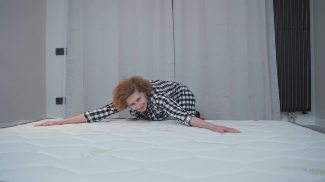Topic is moving to new apartment and buying mattress online for comfortable sleep. Mature woman is happy and tests new mattress on floor in an empty apartment. Healthy sleep on a foam mattress.