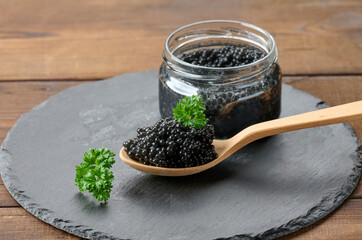 fresh grainy black paddlefish caviar in brown wooden spoon on a brown table, close up