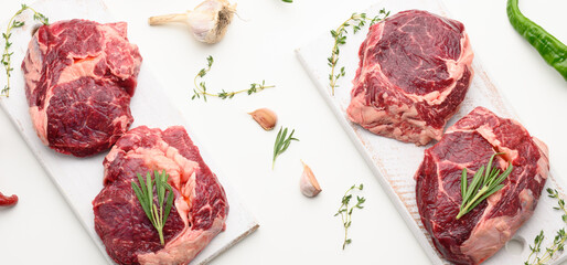 raw piece of beef ribeye with rosemary, thyme on a white table, top view