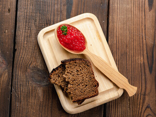 red caviar of pink salmon lies in a wooden spoon on a cutting board. Brown wooden table