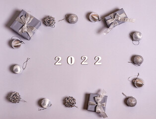 Wooden white numbers 2022 in a frame from gift boxes and New Year's toys on a gray background, copy space.