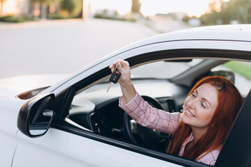 Woman bought first car. Joyful female sitting in new car and shows keys.