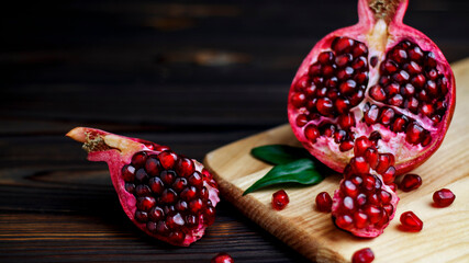 Ripe pomegranate fruit near leaf on dark wooden background