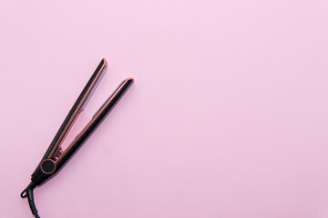 Top view of black hair straightening iron on pink background. Hair care concept
