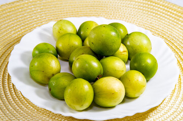 Ripe umbu (Spondias tuberosa) fruits on white plate on rustic surface and selective focus